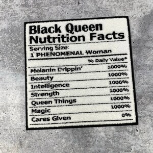 May include: A rectangular rug with a black border, featuring the text "Black Queen Nutrition Facts". The rug lists qualities like "Melanin Drippin'" and "Magic", each with a 1000% value, in black text.