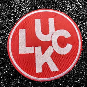 May include: Red circular patch with white embroidered letters spelling "LUCK" in a stylized font.