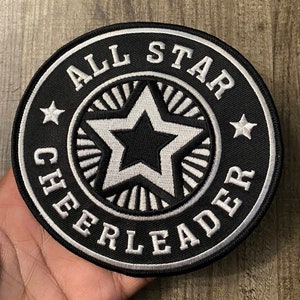 May include: Black and white embroidered patch with the text "All Star Cheerleader" in a circle with a white star in the center.