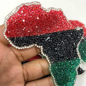 May include: A red, black and green jeweled outline of the continent of Africa. The outline is made of small, faceted rhinestones.