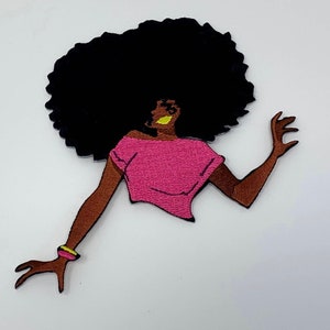 May include: Embroidered patch featuring a stylized Black woman with a large black afro. She wears a pink top and a yellow and pink bracelet. The patch has brown skin and is set against a white background.