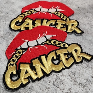 May include: Three red lips with a gold chain and the word "Cancer" in gold letters. The lips are embroidered and have a black outline.