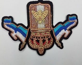 May include: A gold embroidered patch with a beehive design and two blue and white flags on either side. The beehive is decorated with gold and red accents.