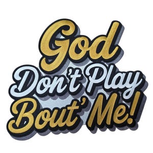 May include: Embroidered patch with the phrase "God Don't Play Bout' Me!" in a stylized, layered design. The text features gold and white lettering with black outlines, creating a 3D effect. The patch is likely for clothing or accessories.