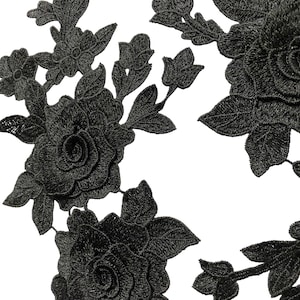 May include: Close-up of black floral lace appliques. The appliques feature detailed embroidered roses, leaves, and smaller flower buds. The intricate design is set against a white background, highlighting the dark, textured fabric.