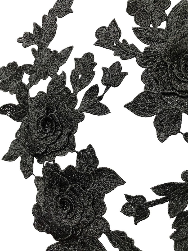 May include: Close-up of black floral lace appliques. The appliques feature detailed embroidered roses, leaves, and smaller flower buds. The intricate design is set against a white background, highlighting the dark, textured fabric.