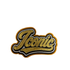 May include: An embroidered patch featuring the word Iconic in a cursive, gold-colored script. The lettering is outlined in black and white thread, with a thick, solid yellow border surrounding the entire design against a plain white background.