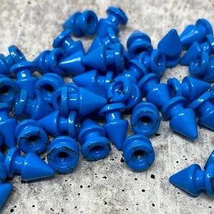 May include: A collection of small, bright blue plastic objects. Each has a conical tip and a cylindrical base with a circular opening. The objects are scattered across a textured surface.