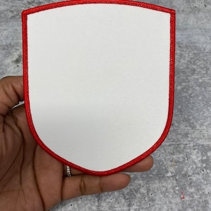 May include: A white, blank patch with a red stitched border in the shape of a shield.