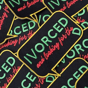 May include: A close-up of several black fabric patches with green and red embroidered text. The text reads "DIVORCED and looking for the D".