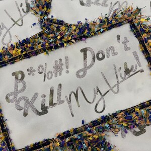 May include: A white fabric pillow with a glittery silver design that says "B*%&#!! Don't Kill My Vibe!" The pillow is trimmed with a colorful fringe.