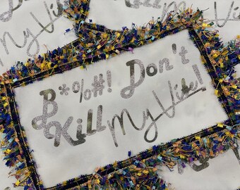 Puede incluir: Una almohada de tela blanca con un diseño plateado brillante que dice "B*%&#!! No mates mi vibra!" La almohada está adornada con una franja colorida.