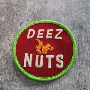 May include: Embroidered patch with a red background and the words "DEEZ NUTS" in white block letters. A cartoon squirrel holding a nut is in the center. The patch has a green border.