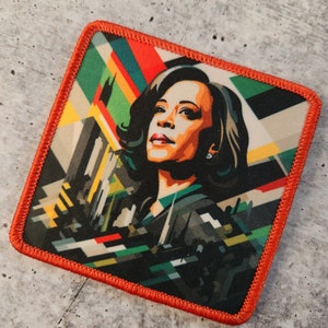 May include: A colourful, abstract patch featuring a portrait of a woman against a dark background. The woman has dark hair and is wearing a dark suit. The patch has a red border.