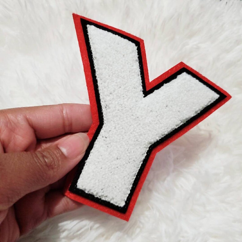 Puede incluir: Letra Y de fieltro blanco con contorno negro y borde rojo. La letra mide aproximadamente 10 cm de alto.