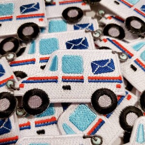 Pu&ograve; includere: Un mucchio di toppe ricamate bianche, blu e rosse che raffigurano un camioncino postale. Ogni toppa ha una busta blu con un bordo bianco sul lato. Il camioncino postale ha ruote nere e una striscia rossa.