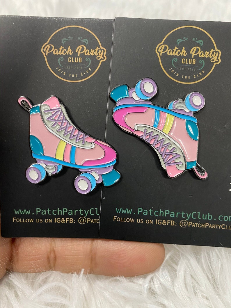 K&ouml;nnte beinhalten: Zwei rosa und blaue Rollschuh-Emaille-Pins mit wei&szlig;en Schn&uuml;rsenkeln und gelben Streifen. Die Pins befinden sich auf einem schwarzen Hintergrund mit dem Text "Patch Party Club" in einem goldenen Kreis.