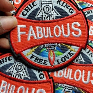 Può includere: Primo piano di un mucchio di toppe ricamate rosse, bianche e nere. Le toppe presentano un razzo, un globo terrestre e le parole "Fabulous", "Chic", "King" e "Free Love".