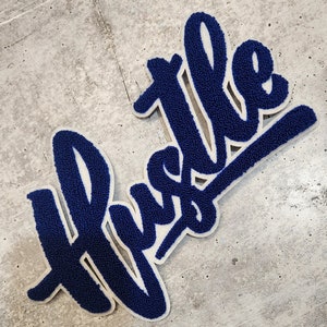 May include: Blue and white felt word art featuring the word "Hustle" in a bold, stylised font.