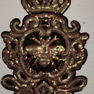 May include: Gold sequined iron-on patch with a crown, ornate design, and a bee in the center.