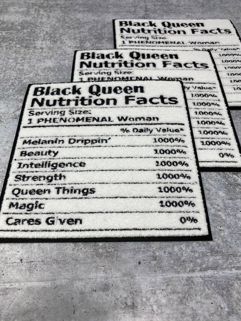 May include: Three rectangular white rugs with black borders. Each rug features the text "Black Queen Nutrition Facts," listing attributes like "Melanin Drippin'," "Beauty," and "Intelligence." The rugs are on a grey surface.