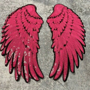 May include: A pair of pink sequined angel wings with black outlines. The wings are made of individual sequins sewn together.