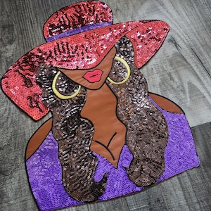 May include: A sequined iron-on patch featuring a woman with long brown hair wearing a large red hat and a purple dress. She has large gold hoop earrings.