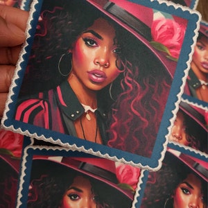 May include: An embroidered patch depicting a woman with dark curly hair wearing a pink hat with a large pink flower. The woman is wearing a red and white striped jacket and a silver necklace.