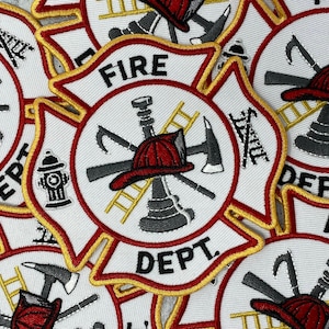 Op de afbeelding: Close-up van verschillende rode, witte en gouden brandweeremblemen met de tekst "FIRE DEPT." in het midden. De emblemen tonen een brandkraan, een ladder, een bijl en een brandweerhelm.