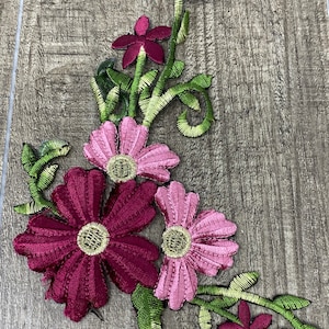 Puede incluir: Aplique floral bordado con flores rosas y burdeos y hojas verdes. El aplique es perfecto para añadir un toque de elegancia a la ropa, los bolsos o los proyectos de decoración del hogar.