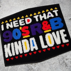 May include: A black patch with the text "I need that 90's R&B kinda love" in colorful, fuzzy letters. The letters are outlined in yellow and the background is black with a red and yellow triangle border.