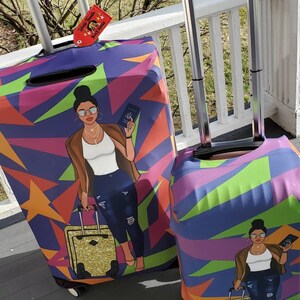 Puede incluir: Dos fundas para maletas con un patr&oacute;n geom&eacute;trico colorido que presenta a una mujer con una chaqueta marr&oacute;n, camisa blanca, jeans azules y gafas de sol sosteniendo un pasaporte y una maleta dorada. El texto "World Traveler Black Girl Magic" est&aacute; en una etiqueta roja unida al asa de una de las maletas.