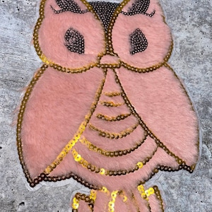 May include: Pink owl applique with gold sequins. The owl has large eyes and a fluffy texture.