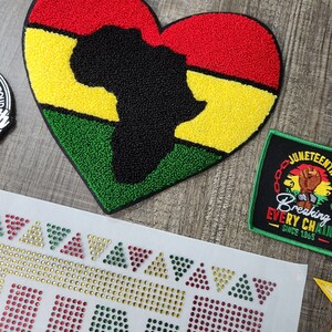 May include: A heart-shaped patch with an outline of the African continent in black, surrounded by red, yellow, and green stripes. The patch is made of a fuzzy material and is perfect for adding a touch of cultural pride to your belongings.