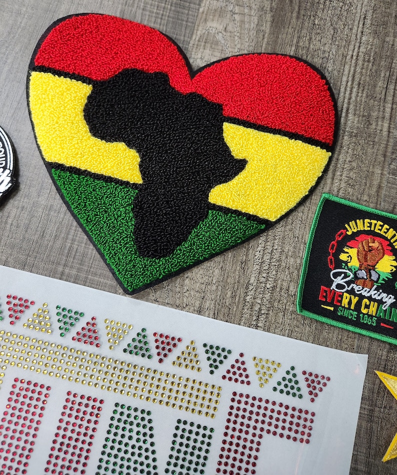 May include: A heart-shaped patch with an outline of the African continent in black, surrounded by red, yellow, and green stripes. The patch is made of a fuzzy material and is perfect for adding a touch of cultural pride to your belongings.