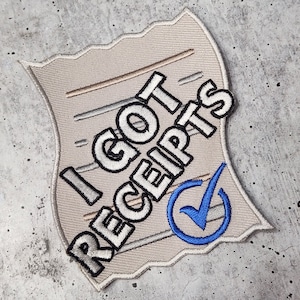 May include: A beige fabric patch with a white checkmark in a blue circle. The patch has the text "I GOT RECEIPTS" in white letters.