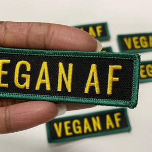 May include: A black and green embroidered patch with the text "VEGAN AF" in yellow thread.
