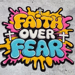 Op de afbeelding: Een kleurrijk geborduurd patch met de woorden "Faith Over Fear" in een vet, graffiti-achtig lettertype. De patch is omgeven door een roze en geel splatterontwerp.