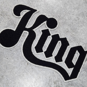 May include: Black and white "King" logo with a stylized font. The logo is on a gray textured surface.
