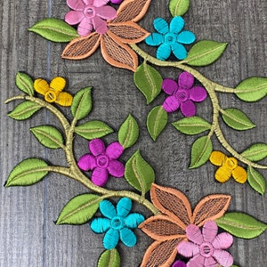 May include: Two embroidered floral appliques with green leaves, orange, pink, purple, yellow, and blue flowers.