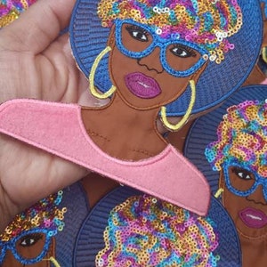 Könnte beinhalten: Ein Set bunter gestickter Bügelbilder mit einer Frau mit blauer Brille und einem blauen Afro. Die Patches haben ein glitzerndes, paillettenbesetztes Design.