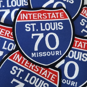 May include: A close-up of several blue and red interstate highway signs with white text. The signs read "Interstate 70 St. Louis Missouri".