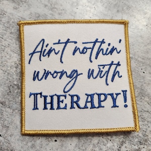 May include: White square patch with gold stitching around the edges. The text "Ain't nothin' wrong with THERAPY!" is embroidered in blue.