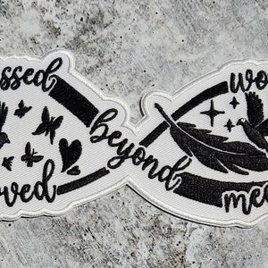 May include: White infinity symbol embroidered patch with black stitching. The left side features a bird, butterflies, and a heart with the text "Missed Loved beyond". The right side features a bird, a feather, and a branch with the text "words measure".