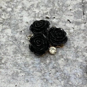 Op de afbeelding: Drie zwarte rozen met een gouden basis en een enkele strass in het midden.