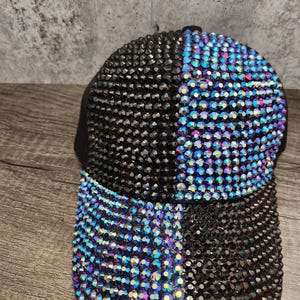 May include: A black baseball cap with a blue and black rhinestone design. The rhinestones are arranged in a checkered pattern.