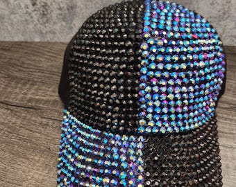 May include: A black baseball cap with a blue and black rhinestone design. The rhinestones are arranged in a chequered pattern.