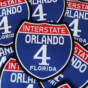 May include: Multiple blue and red interstate highway signs with white text. The signs read "Interstate Orlando 4 Florida".