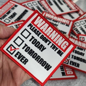 May include: A white patch with a red border and the text "WARNING! PLEASE DON'T TRY ME" with a checklist below. The checklist has three options: "TODAY", "TOMORROW", and "EVER". The option "EVER" is checked.