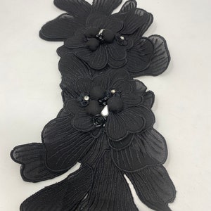 May include: Black fabric flower applique with beaded embellishments. The applique features two large flowers with layered petals and a smaller flower in the center.